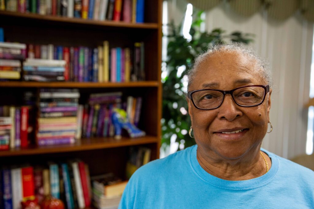 Dorothy, Senior at Buena Vista Senior Community Volunteers of America Michigan standing in front of a book case, smiling.